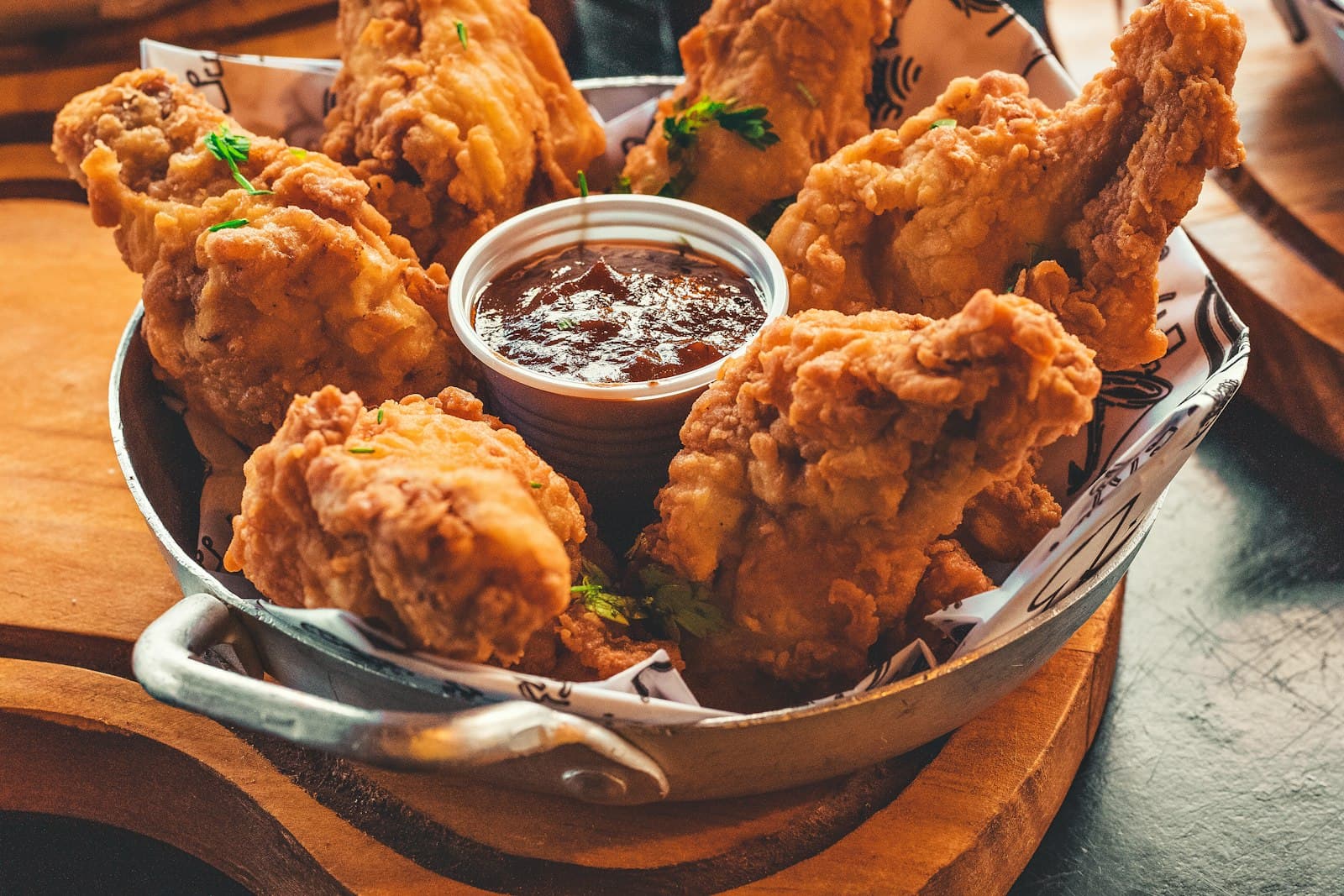 Golden crispy fried chicken pieces in a metal basket with a small bowl of dipping sauce