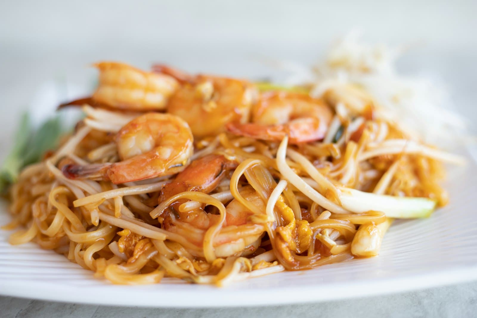 Shrimp pad thai with rice noodles, scrambled egg, bean sprouts and green onions on a white plate