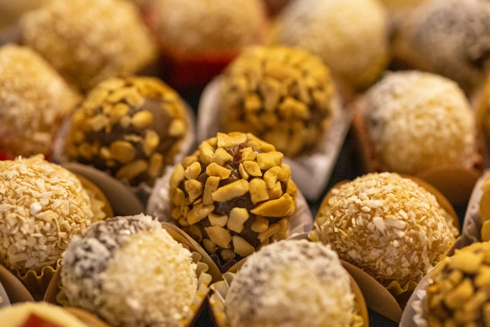 Round chocolate truffles coated in chopped nuts and shredded coconut, sitting in paper cases