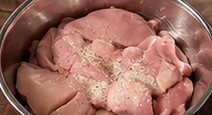 Raw boneless chicken pieces seasoned with salt and pepper in a steel mixing bowl