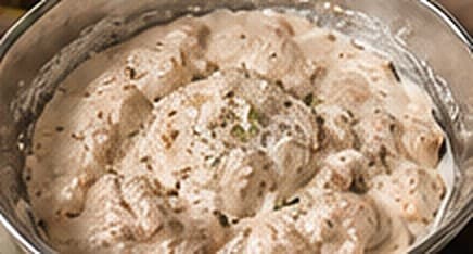 Chicken pieces coated in a creamy yogurt and spice marinade in a steel bowl