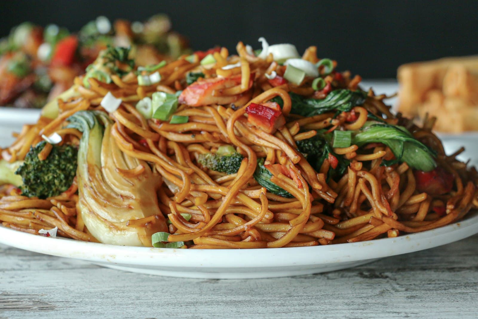 A plate of stir-fried noodles with bok choy, broccoli, red pepper and green onions