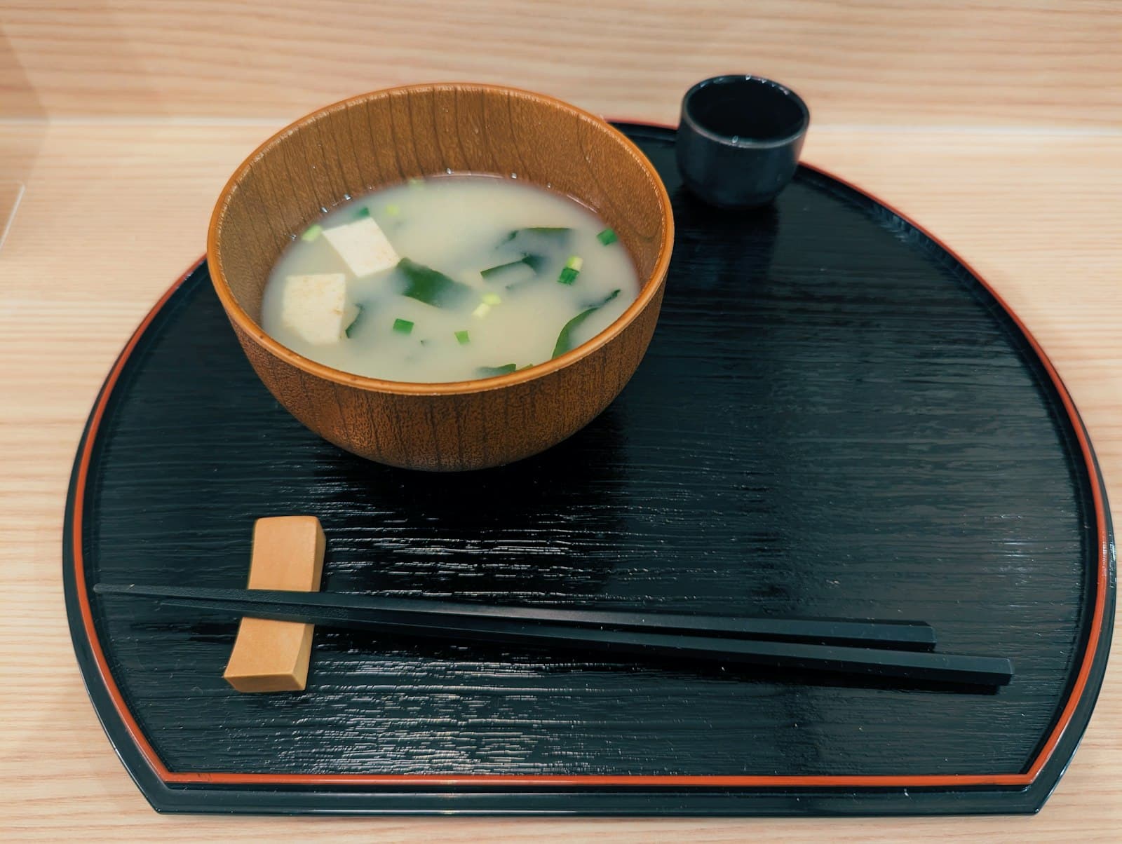 Miso soup with cubes of tofu, wakame seaweed and green onions in a wooden bowl on a black lacquered tray with chopsticks