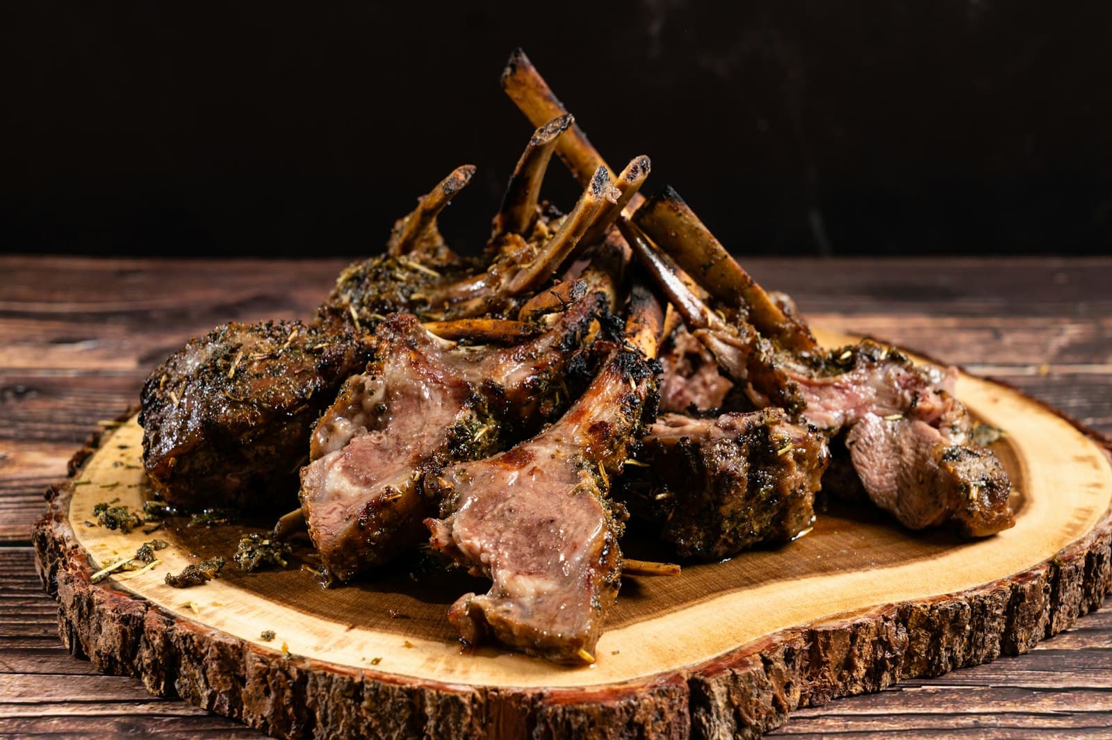 Herb-crusted lamb chops piled on a round wooden serving board, pink in the centre